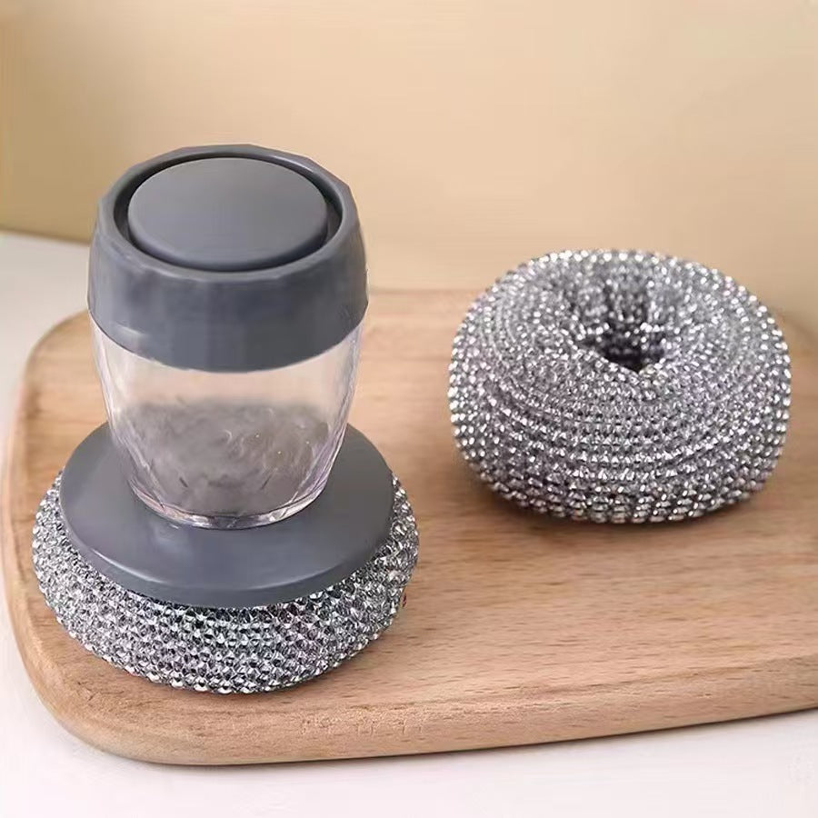 Soap dispenser with gray lid and base, and metallic scrubber on a wooden board.