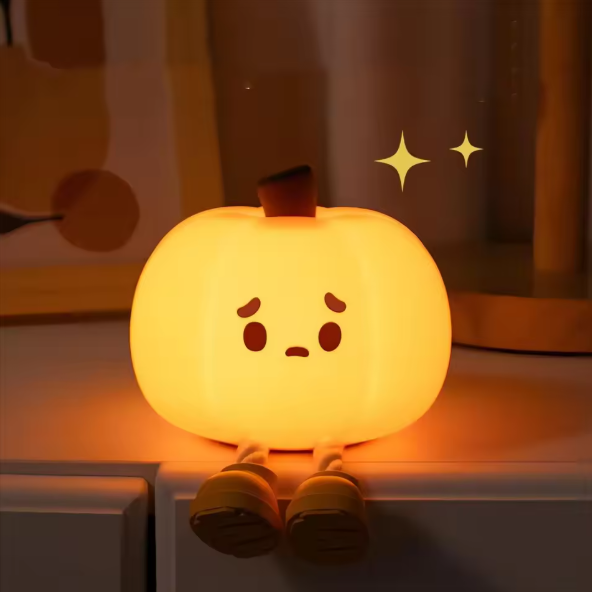 Cute pumpkin-shaped night light with a sad face on a wooden surface.