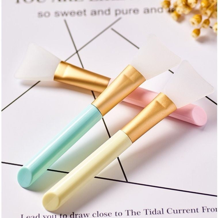 Three colorful facial silicone mask brushes with gold accents on a white background