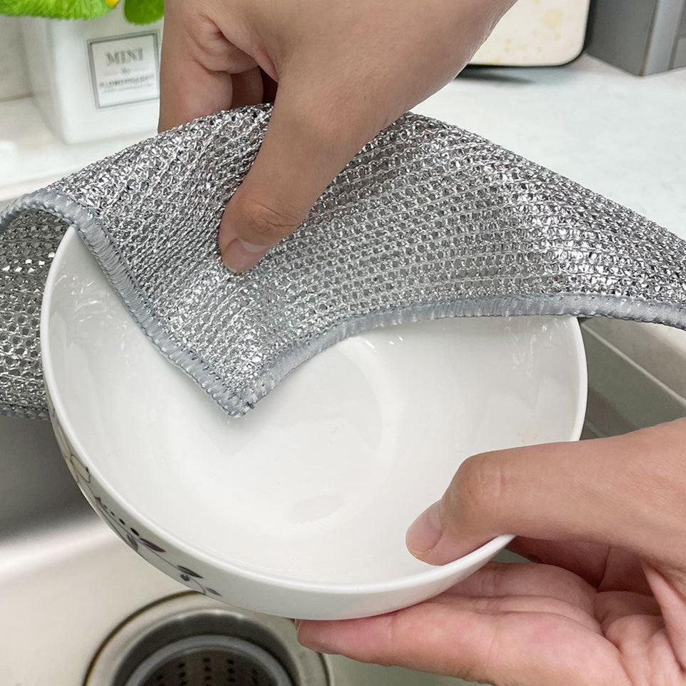 Person cleaning a white bowl with a metallic scrubber in a kitchen setting.