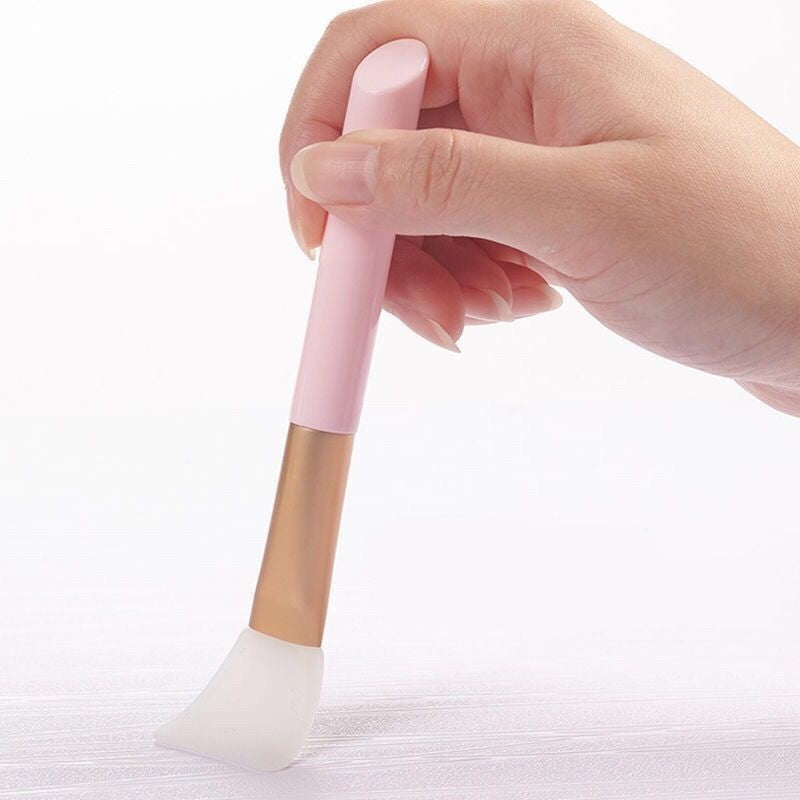 Hand holding a pink and gold facial silicone mask brush on a white background