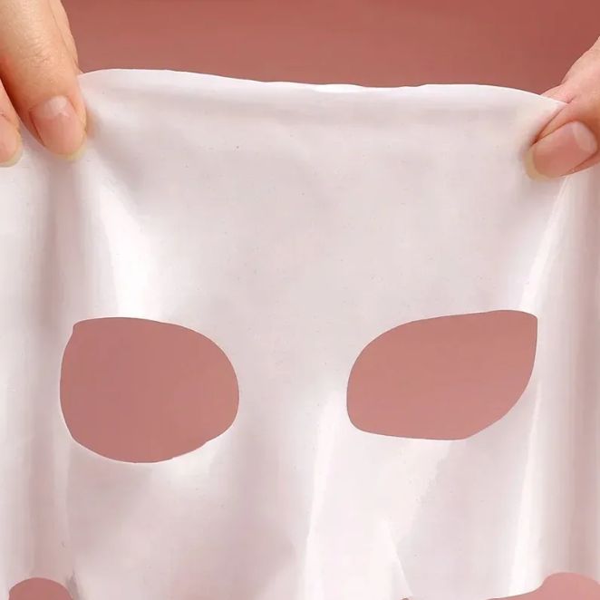 Bio-collagen Face Mask on a white cloth held by hands against a pink background